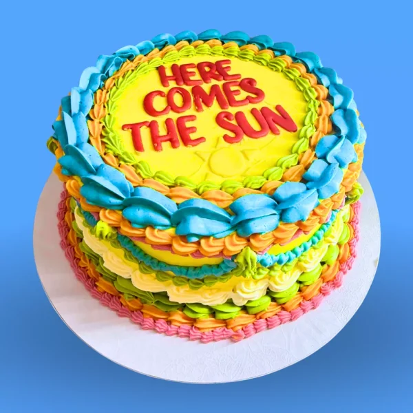 Gâteau coloré personnalisé "Here Comes The Sun" avec glaçage arc-en-ciel, idéal pour anniversaire ou fête, cake artisanal original Genève Lausanne